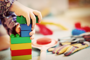 Mão de uma criança brincando com cubos de madeira coloridos